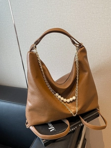 Brown faux leather tote bag with gold chains and pearl charms shown in a lifestyle setting