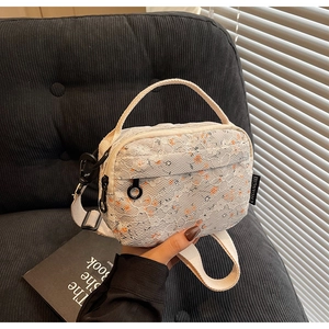 Detail of floral crossbody bag with white lace overlay and orange flowers on orange base