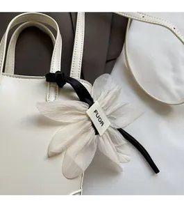 Vue détaillée du sac à main minimaliste en cuir blanc avec grand charme de fleur en tissu