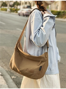 Brown nylon crescent crossbody bag shown on a model in an urban outdoor setting