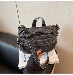 Detail of dark grey denim crossbody bag with vintage washed texture and multi-zipper design