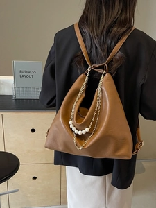 Brown leather versatile tote bag with gold chain pearl charm worn by model in business setting