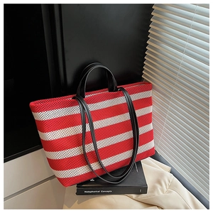 Détail d'un cabas en mesh à rayures rouges et blanches avec poignées en cuir noir sur un bureau