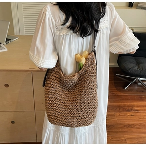 Brown woven straw tote bag with long straps worn by a model in a modern office setting
