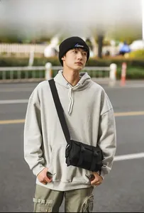 Outdoor street style shot of a black messenger bag with buckle detail and crossbody strap