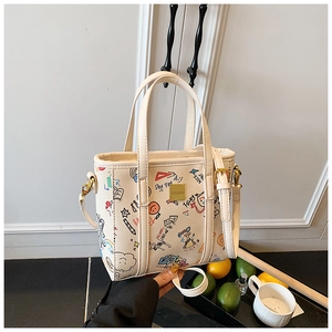 Detail of cream white tote bag featuring colorful graffiti prints and golden hardware