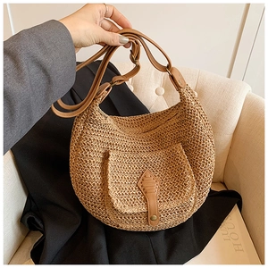 Detail shot of the woven straw texture and premium brown leather buckle on a hobo bag