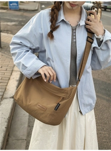 Outdoor shot of a tan waterproof nylon crossbody bag with adjustable wide strap