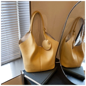 Detailed view of yellow lychee textured tote bag with round charm on a black book