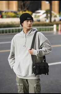 Detailed view of the black nylon messenger bag with buckle strap on a grey hoodie