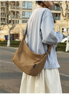 Close-up of brown nylon half-moon crossbody bag with leather brand patch and wide strap