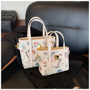 Detail view of two white leather bucket bags with colorful graffiti prints on a leather surface