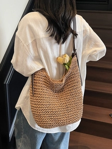 Handcrafted straw tote bag with brown leather straps shown on model back on wooden steps
