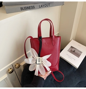 Détail du sac seau rouge avec breloque fleur en tissu blanc et finition mate lisse