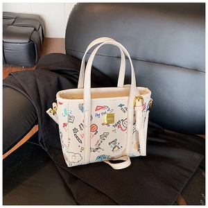 Detailed shot of cream tote bag with colorful graffiti prints and golden metal logo plate