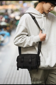 Outdoor street style shot of a black cylindrical messenger bag with adjustable strap