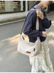Close-up of off-white nylon crescent crossbody bag with brown leather logo patch details