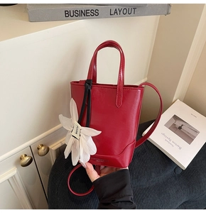 Détail du sac seau rouge en cuir avec breloque fleur blanche et poignée