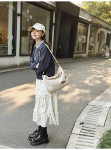 Detail view of a cream canvas messenger bag with leather accents in city street setting