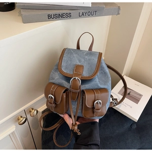 Detail of blue denim backpack with brown leather trim and silver buckle hardware
