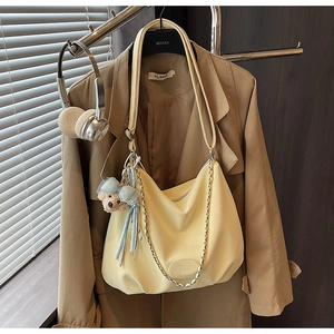 Detail of pale yellow leather tote with teddy bear charm and metal chain accessory