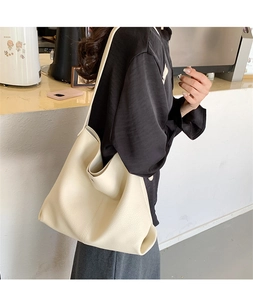 Detail of off-white tote bag with litchi grain texture worn by a model in a modern cafe