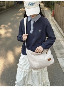 Waterproof nylon crossbody bag in light khaki shown on a model in an outdoor street setting