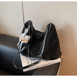 Detail of black tote bag featuring vertical texture, silver chain, and cute blue bear charm