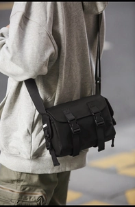 Street style shot of a black messenger bag with matte finish and buckle closure