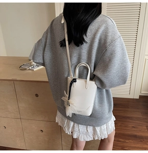 Détail du sac seau minimaliste blanc avec pendentif fleur et bandoulière amovible