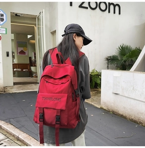 Detail of red canvas backpack featuring black buckle closure and embroidered lettering logo