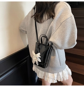 Détail du sac seau en cuir verni noir brillant avec breloque fleur blanche et bandoulière