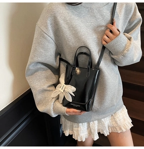 Détail du sac seau en cuir verni noir brillant avec breloque fleur en soie et logo