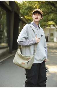 Detailed view of khaki nylon messenger bag with leather label in an outdoor street style setting