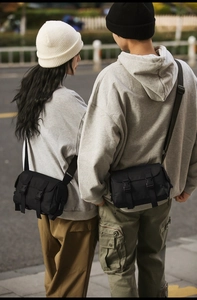 Rear view of a couple wearing black urban techwear messenger bags in a street setting