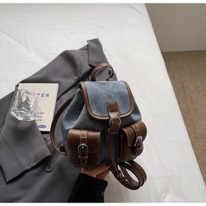 Detail of blue denim backpack with brown leather trim and silver metal buckles