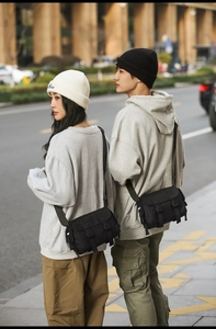 Outdoor shot of a black tactical messenger bag with adjustable buckles worn by a person