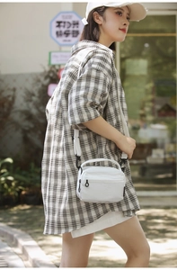 Detailed outdoor view of a white crossbody bag with checkered texture and wide strap
