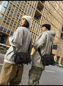 Close-up of black street style messenger bag with dual buckles and adjustable strap