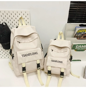 Detail showing two sizes of off-white canvas backpacks with black buckles and yellow straps