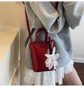 Mini sac seau rouge en cuir avec breloque fleurie porté en bandoulière par un mannequin