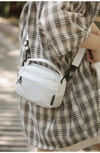 Detailed shot of white textured crossbody bag with zip pockets on a casual checkered shirt