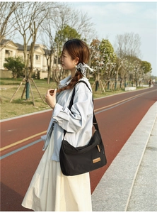 Detail of water-resistant black nylon messenger bag with brown leather logo patch