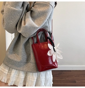 Détail du sac cabas en cuir verni rouge avec grand pendentif fleur blanche sur mannequin