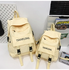 Detail view of cream canvas backpacks in two sizes with buckle straps and embroidery