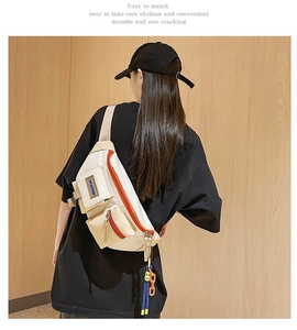 Vue détaillée du sac bandoulière crème à poches multiples avec zips orange et breloque