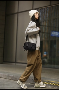 Close-up of a black canvas messenger bag featuring dual buckle straps on a street model