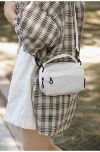 Detailed outdoor shot of white grid texture crossbody bag with black dual zippers