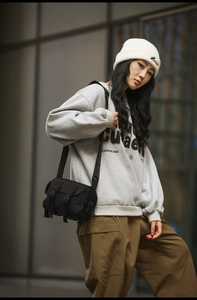 Detailed view of black nylon messenger bag with buckle closure worn by male street model