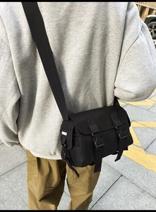 Street style shot of a black nylon messenger bag with buckle closure and wide shoulder strap